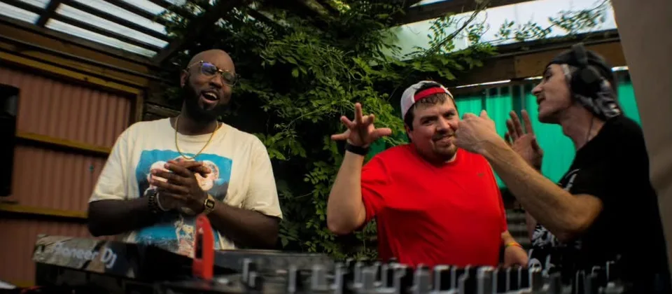 Three DJs laughing behind the decks on the patio at The Spot