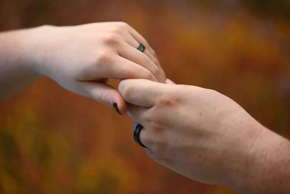 Two hands with wedding rings against autumn leaves