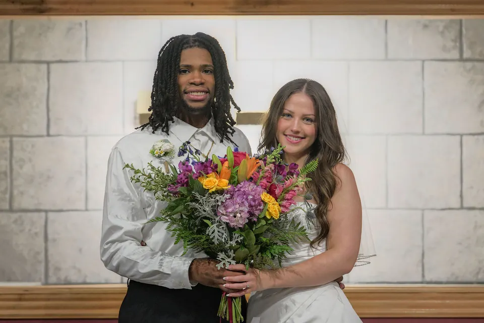 Kassie and Noah with the bouquet in front of a stone wall