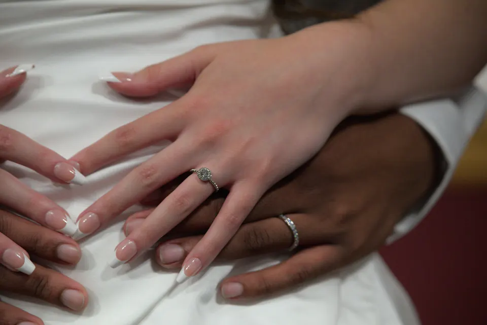 Hands with wedding rings resting on a white dress